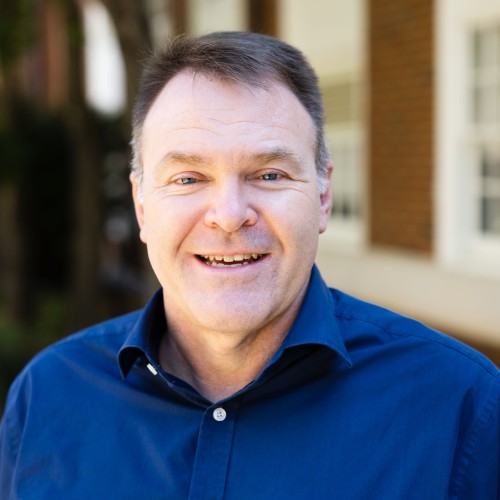 A man wearing a blue shirt smiles warmly at the camera.