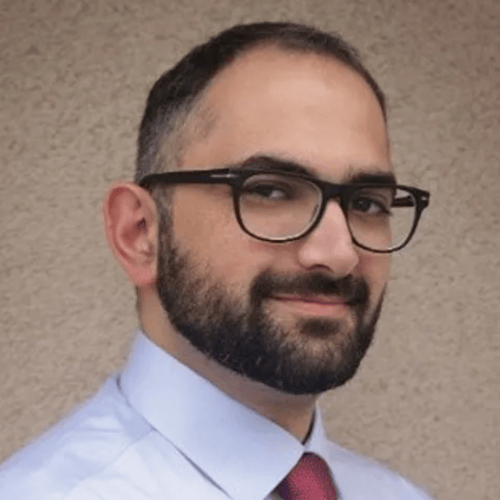 A man with glasses and a beard, dressed in a tie, poses confidently for the camera.